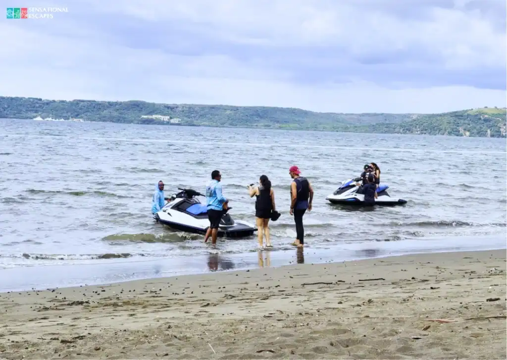 Turistas y guías se preparan para conducir jet skis a lo largo de la orilla tranquila de Playa Panamá, Guanacaste, con colinas verdes al fondo.