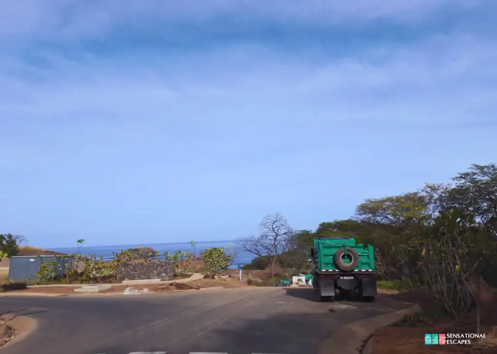 Carretera asfaltada hacia Playa Calz&oacute;n de Pobre en Guanacaste, Costa Rica, con un cami&oacute;n verde estacionado cerca de un peque&ntilde;o parqueo y el oc&eacute;ano a lo lejos.