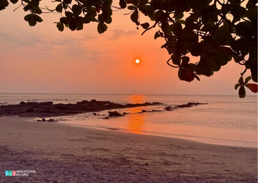 Vibrant orange sunset reflecting on calm ocean waters with rocky shoreline and sandy beach at Playa Blanca.