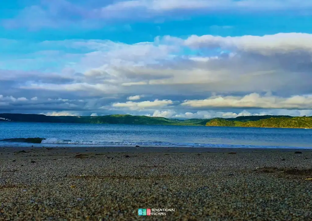 Vista desde la arena en Playa Buena hacia las colinas verdes de Bah&iacute;a Culebra bajo cielo parcialmente nublado.